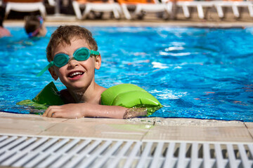 Little boy swims independently in a large pool in special glasses and sleeves of green color....