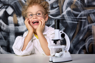 Joyful five-year-old child works with microscope in biology and chemistry class in children's lab....