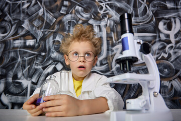 An inquisitive child enthusiastically looks at the microscope while sitting at a table with test...