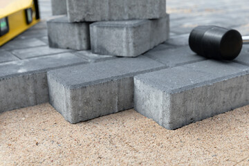 Laying cement pavement on a walkway with a rubber hammer and gloves on a sand. House improvement.
