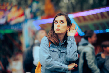 Funny Woman Trying to Overhear a Discussion in a Public Space. Curious girl hearing an announcement made in a local funfair 
