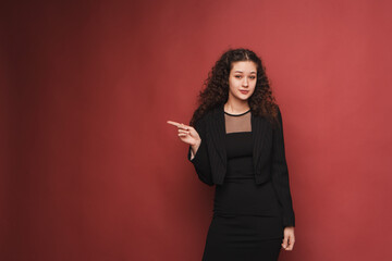 fashion female portrait. Girl, curly girl with black hair in a strict business suit on a red, pink background. High quality photo