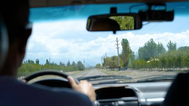 A man drives down the road in Mendoza, Argentina in slow motion. Camera slides outf rom the headrest.