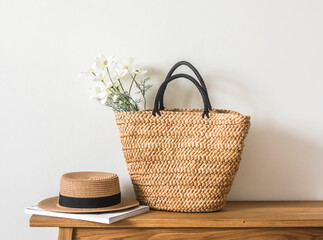 A wicker straw summer bag, a hat and a magazine on a wooden bench. Summer season - obrazy, fototapety, plakaty