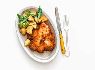 Chicken schnitzel with crispy potatoes and rocket salad jy the light background top view