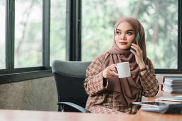 The cheerful and joyful millennial Asian Muslim woman is enjoying listening to music through her...