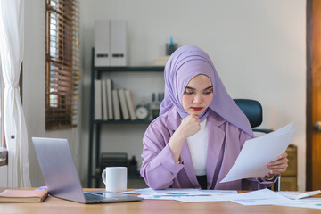 Stressed Muslim millennial businesswoman wearing a purple hijab working from home on laptop looking worried, tired and overwhelmed.