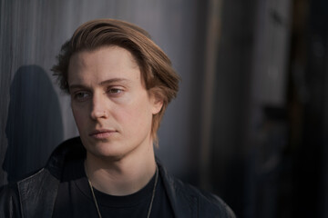 Fototapeta premium A genderfluid model (he, she, they) wears a black leather jacket and stands in front of a gray wall, looking into the distance.