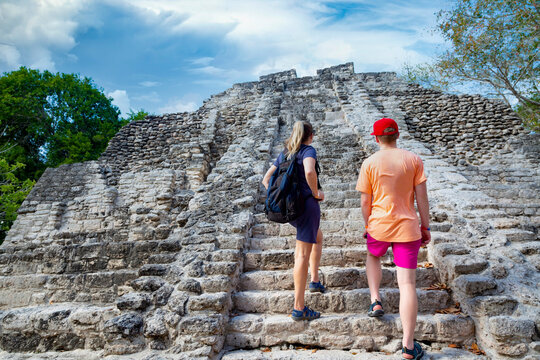 Two Adult Tourists climbing the stairway of large Mayan temple ruins while on vacation. View from behind with large stone steps leading up to the top of the Mayan Temple