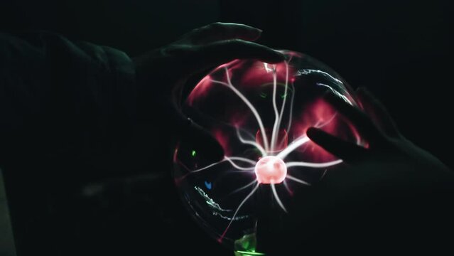 People touch a glass ball with glowing electric discharges inside with their hands