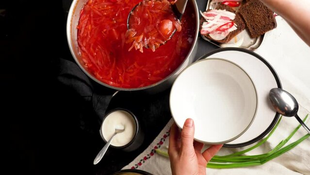 Woman holding clay bowl with Ukrainian borsch. Traditional Ukrainian Russian borscht with white beans on the bowl. Plate of red beet root soup borsch on black rustik table. Beetroot soup Top view