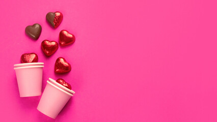 Wrapped and unwrapped heart shape chocolate candies in red foil on pink background