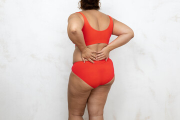 Naked overweight woman touch back with hands, white background. Woman in red underwear with...