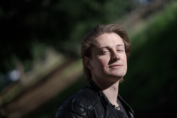 A young gender-fluid model (he / she / they) stands for an outdoor portrait, with dramatic lighting. With their head tilted upwards, they gaze at the camera, expressing confidence and pride.