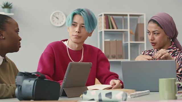 Young multiethnic team of software engineers chatting at office desk while developing new vr game or program together