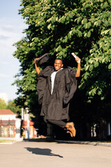 Happy african american graduate from university bouncing with happiness in black mantle and hat....