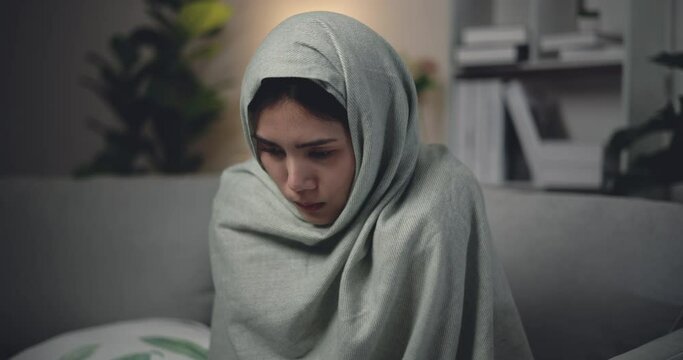 Footage of Sick young Asian woman in warm blanket shiver tremble with cold sitting on sofa at living room. People, health care and lifestyle concepts.