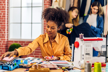 Fototapeta premium Portrait of young african american woman fashion designer stylish sitting and working with color samples.Attractive young african girl work with colorful fabrics at fashion studio