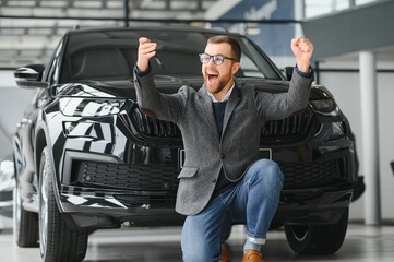 Happy owner of a new car. Emotional handsome man in casual clothes is happy, buying a car in the dealership.