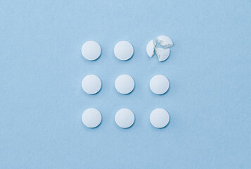 White round pills arranged in square order and one of them is crushed on parts.