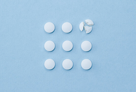 White round pills arranged in square order and one of them is crushed on parts.