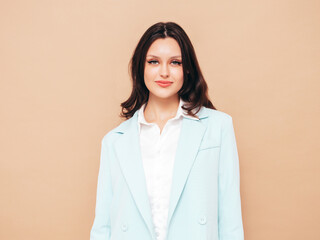 Portrait of young beautiful brunette woman wearing nice trendy blue suit jacket and jeans. Sexy fashion model posing in studio. Fashionable female isolated on beige. Cheerful and happy