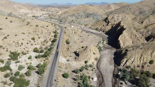 Aerial drone zoom in shot over a vehicle parked alongside a winding RCD Road surrounded by arid vegetation in Balochistan at daytime.