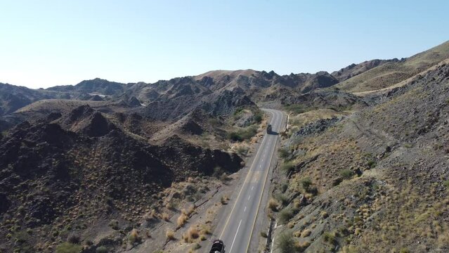 Aerial drone following shot over truck driving along winding RCD Road surrounded by mountain range in Balochistan. Tracking.