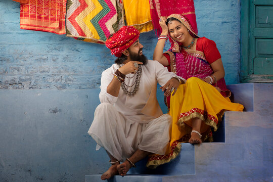 Rajasthani couple sitting on stairs sharing a light moment, as the husband plays ektara