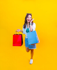Pretty Asian woman in trendy summer fashion is smiling and holding shopping bags in happiness for discount sale isolated on yellow background for advertising and promotion event concept