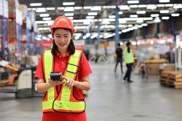 Warehouse workers woman with hardhats and reflective jackets while holding scanner barcode and looking at camera with production stock and retail warehouse logistics distribution center background