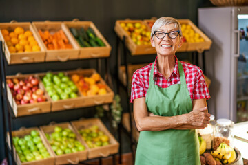 Mature woman works in fruits and vegetables shop. Portrait of small business supermarket owner.