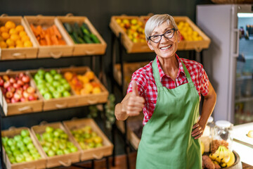 Mature woman works in fruits and vegetables shop. Portrait of small business supermarket owner.
