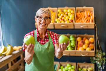 Worker in fruits and vegetables shop is holding apples.