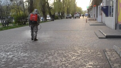 Man in protective suit spraying antiseptic solution on sidewalk in city. Persona disinfecting spray chemicals to preventing spread coronavirus. Sanitary measures in public place. Coronavirus pandemic