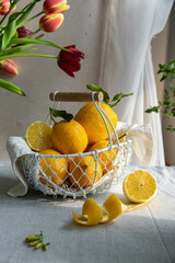 Fresh lemons in white wire basket on bright background in warm light.