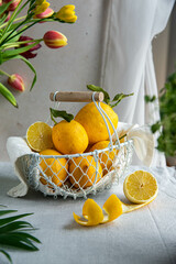 Fresh lemons in white wire basket on bright background in warm light.