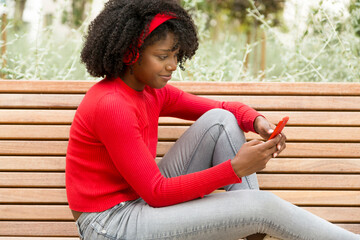 Smiling Afro woman on bench using mobile phone