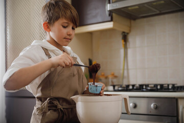 Family activities for kids at home. Preteen boy makes homemade cupcakes at domestic kitchen. Child baking muffins.