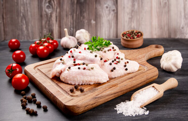 Raw chicken wings with ingredients for cooking on a wooden cutting board on a dark background.