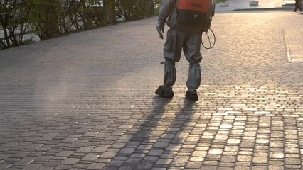 Man in protective suit spraying antiseptic solution on sidewalk in city. Persona disinfecting spray chemicals to preventing spread coronavirus. Sanitary measures in public place. Coronavirus pandemic