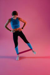 Fototapeta na wymiar Athletic woman trains legs with fitness elastic band on studio background. High quality photo