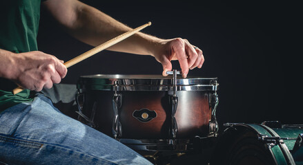 A man plays the snare drum against a dark background.