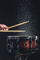 Drummer using drum sticks hitting snare drum with splashing water.