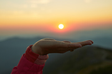 Sun over female hand. Sunrise in mountains. Ready for adventure. Natural mountain landscape with illuminated misty peaks, foggy slopes and valleys
