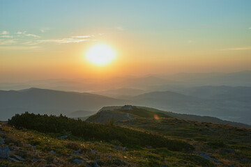 Obraz premium Sunrise in mountains. Natural mountain landscape with illuminated misty peaks, foggy slopes and valleys, blue sky with orange yellow sunlight
