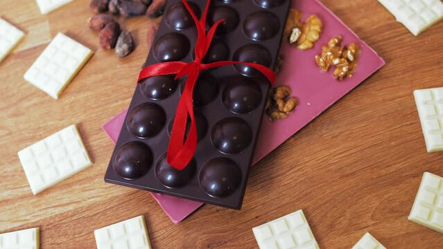 Ruby white and dark chocolate bar with a red bow on a plate. Fruit and nuts chocolate bar with cacao beans on a wooden table. High-quality 4k footage