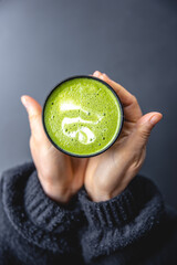 Top view of woman holding in hands trendy green matcha drink with latte art.