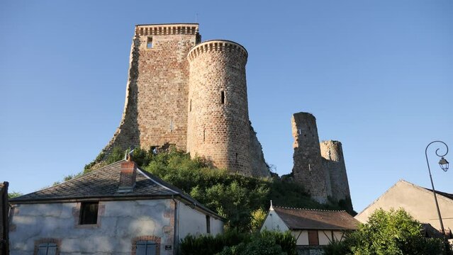 View of ruined tower and walls of ancient fortified castle rising on hilltop above residential buildings of Herisson township in France on sunny summer day. High quality 4k footage