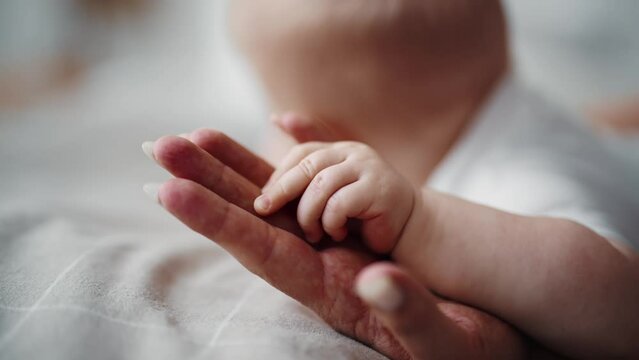 Baby touches mommy's hand grasping reflex of infants, affection formation, hands close-up view. Newborn child holding hand of mother. Childhood motherhood, babycare and kid's protection concept.